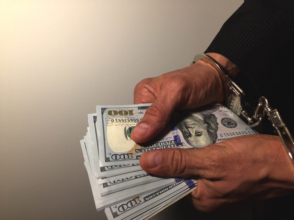 Man in handcuffs holding dollar notes